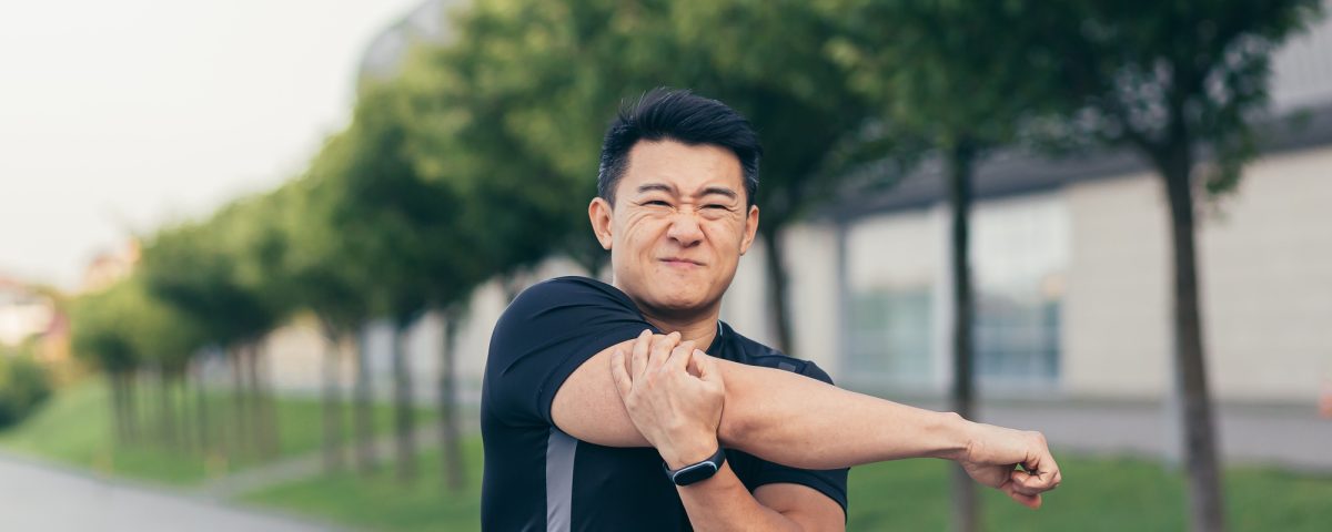 Male asian athlete, kneading shoulder pain, sore arm muscles in the park