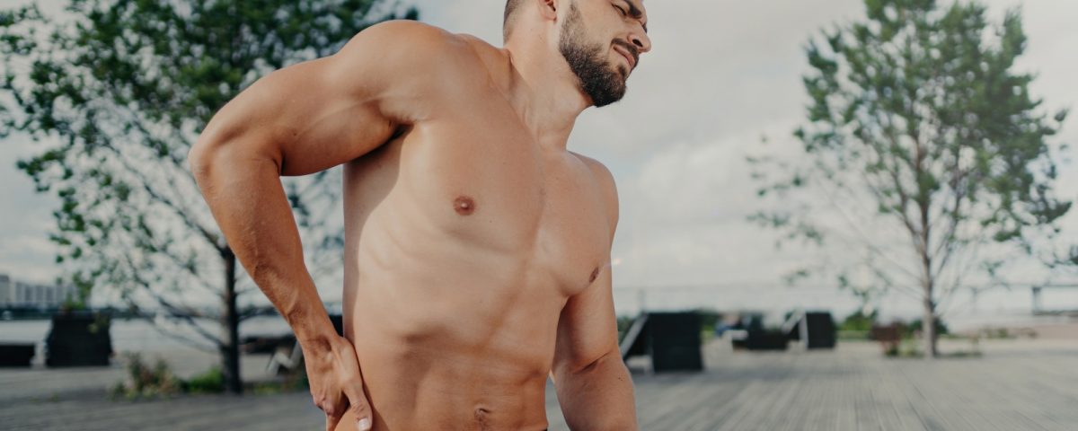 Unshaven sportsman: lower back pain after training. Outdoor poses. Exercise injury