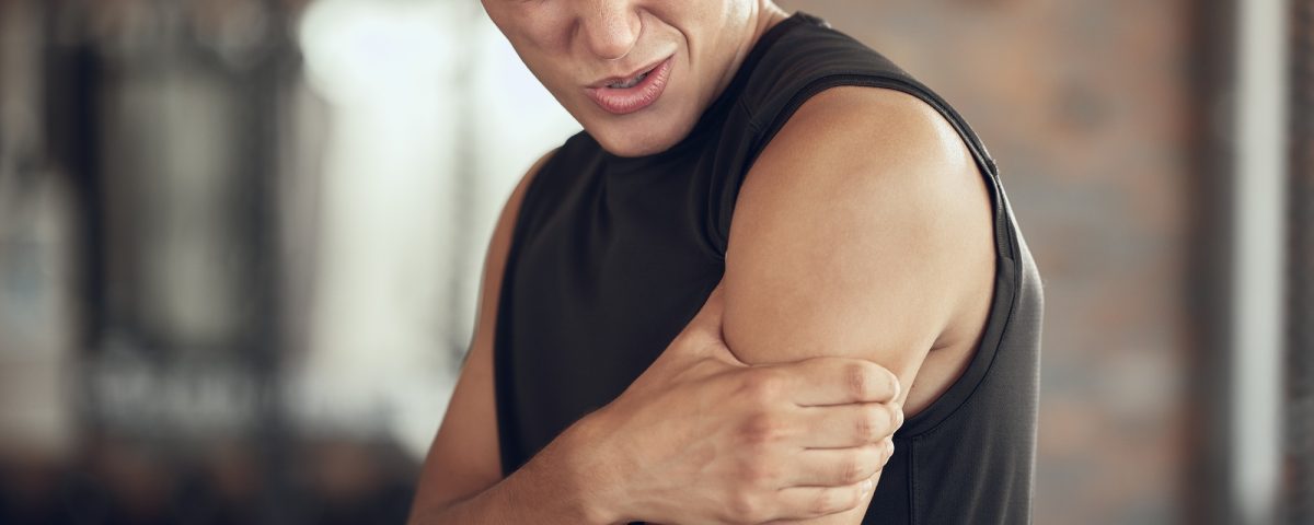 Young athlete with a stiff arm in the gym. Bodybuilder feeling bicep pain in the arm. Young fit man